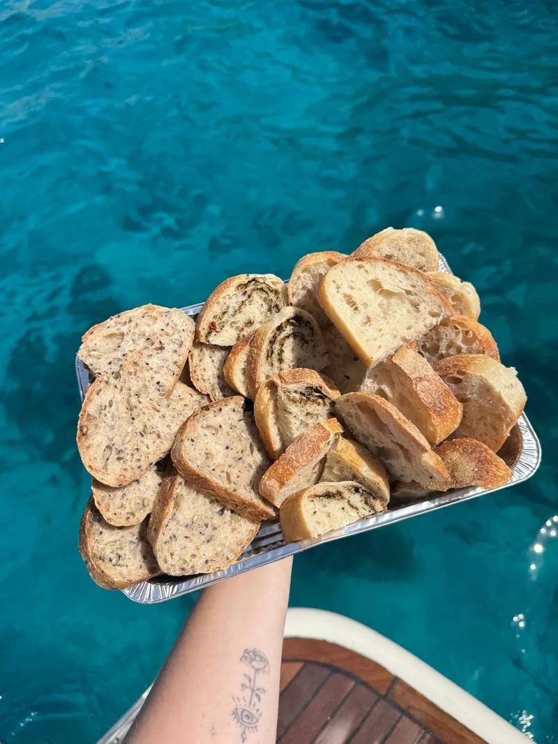 A tray of sliced plain, seeded and pesto-swirl sourdough held over turquoise sea